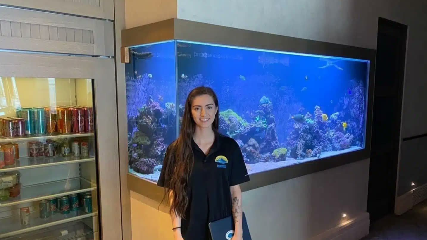 An aquarium service specialist standing beside a large built-in reef aquarium